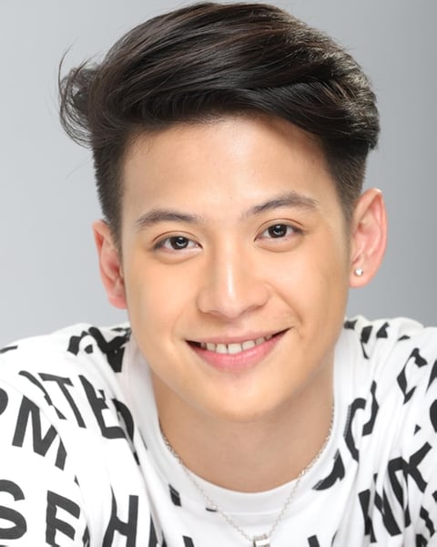 Smiling young man with dark styled hair wearing a white and black patterned shirt against a gray background
