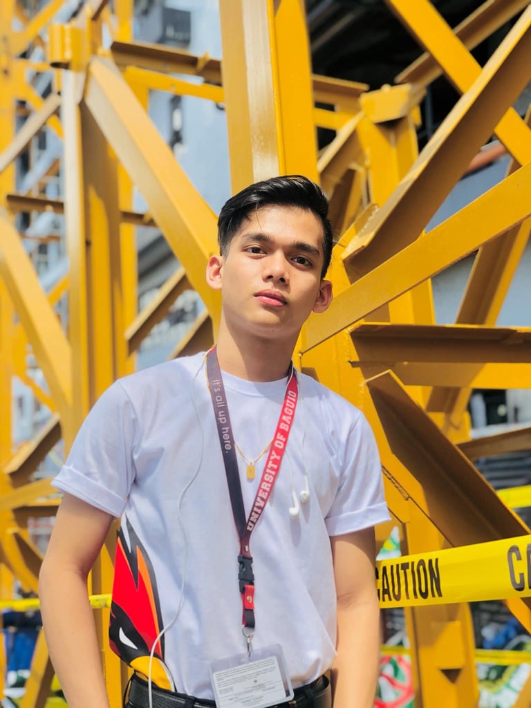 Young man wearing white t-shirt and ID badge standing in front of large yellow metal structural framework