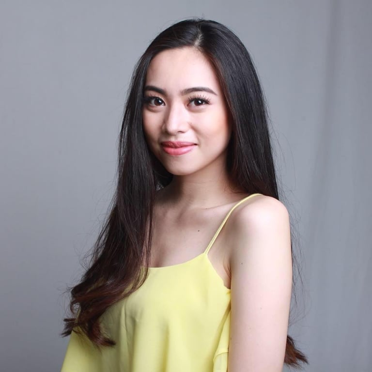 Portrait of a young woman with long black hair wearing a yellow camisole against a gray background