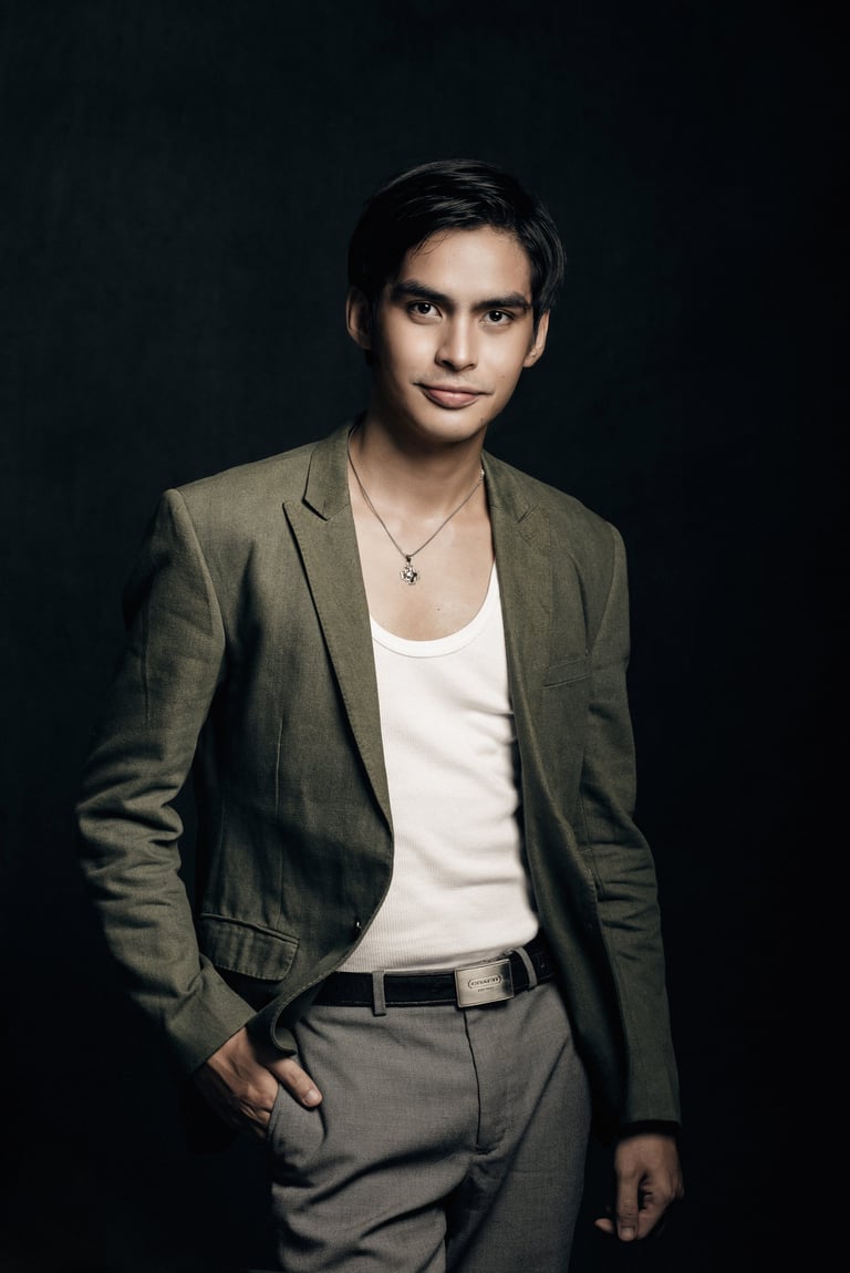 Young man in olive blazer and white shirt with cross pendant against dark background
