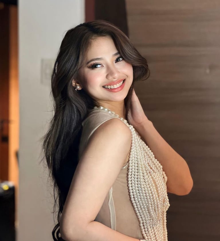 Woman with long black hair smiling and posing over shoulder, wearing a beaded white sleeveless top