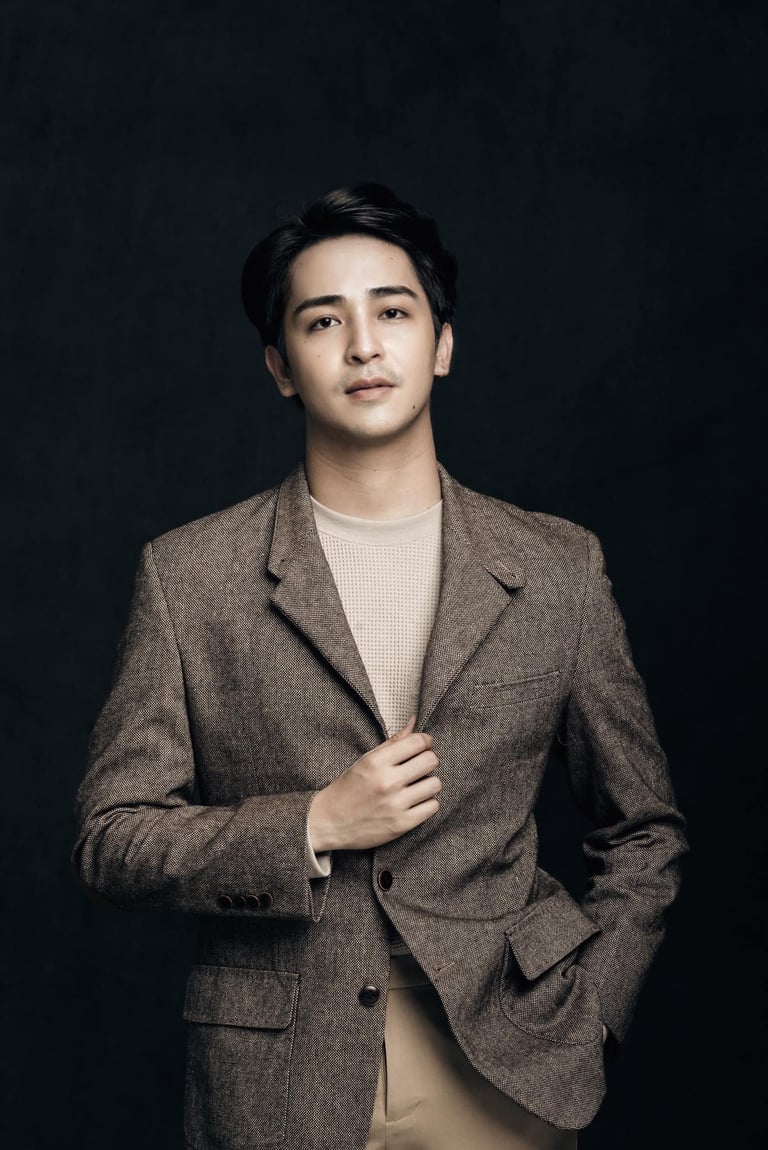Professional portrait of an Asian man wearing a brown tweed blazer over a cream sweater against a dark background