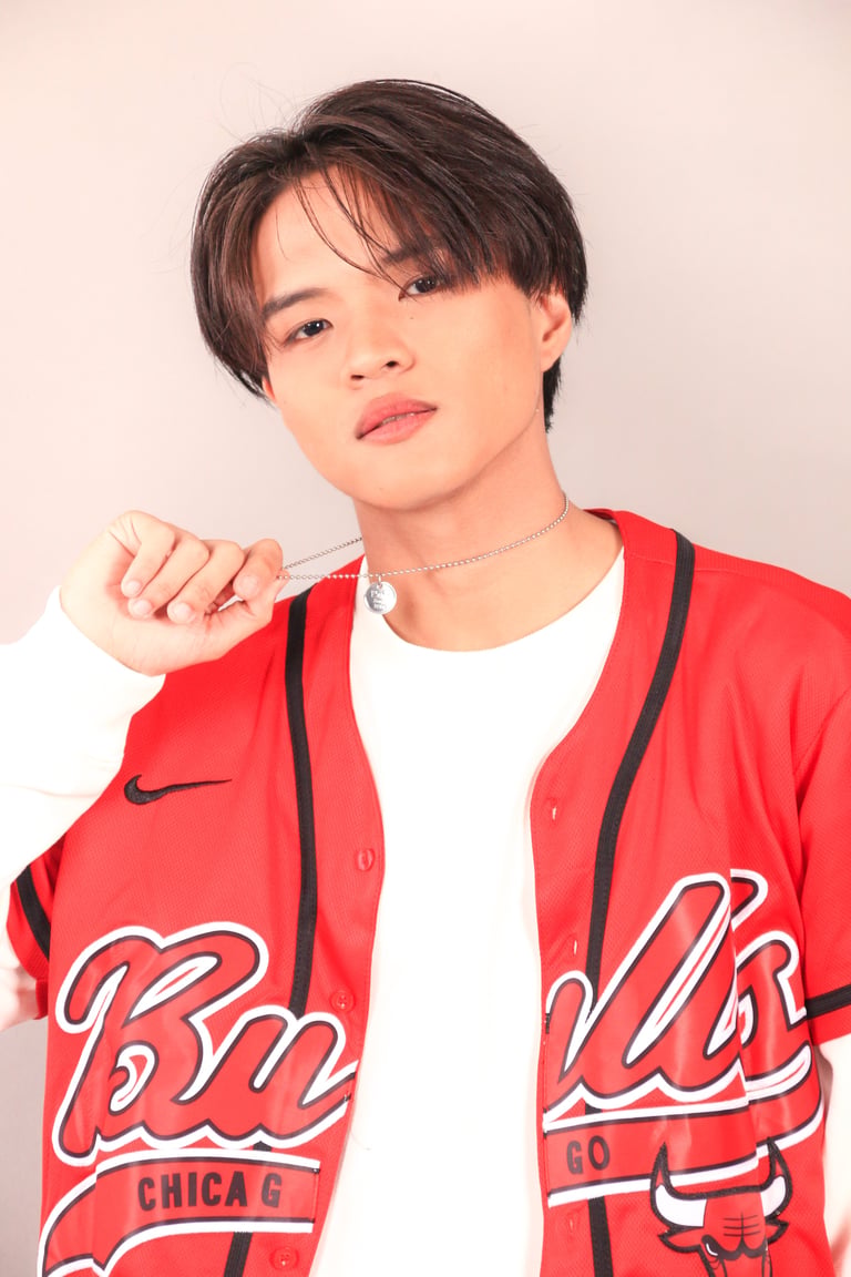 Young man wearing red Chicago Bulls basketball jacket over white shirt, posing against neutral background