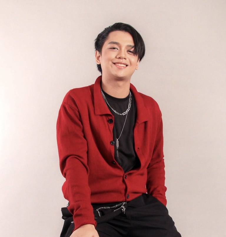Smiling young person wearing a red cardigan over a black shirt with silver chain necklaces against a neutral background