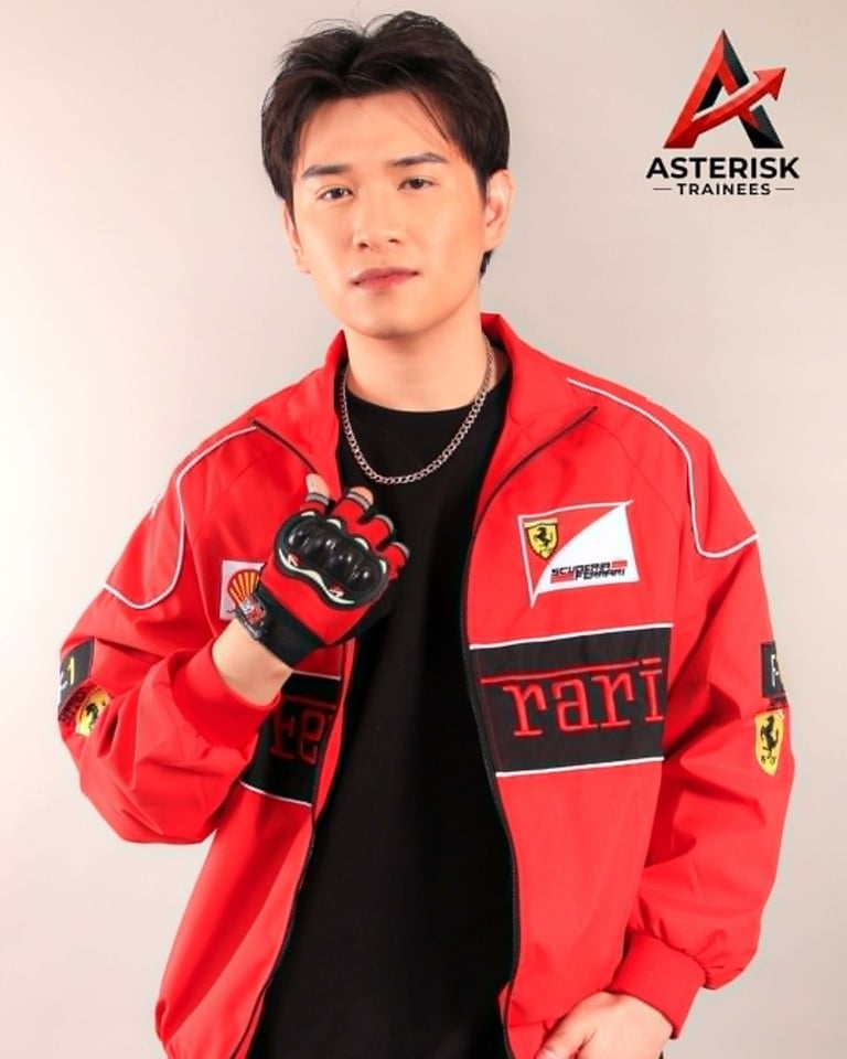 Young man wearing red Ferrari racing jacket with black gloves, posed against white background with Asterisk Trainees logo