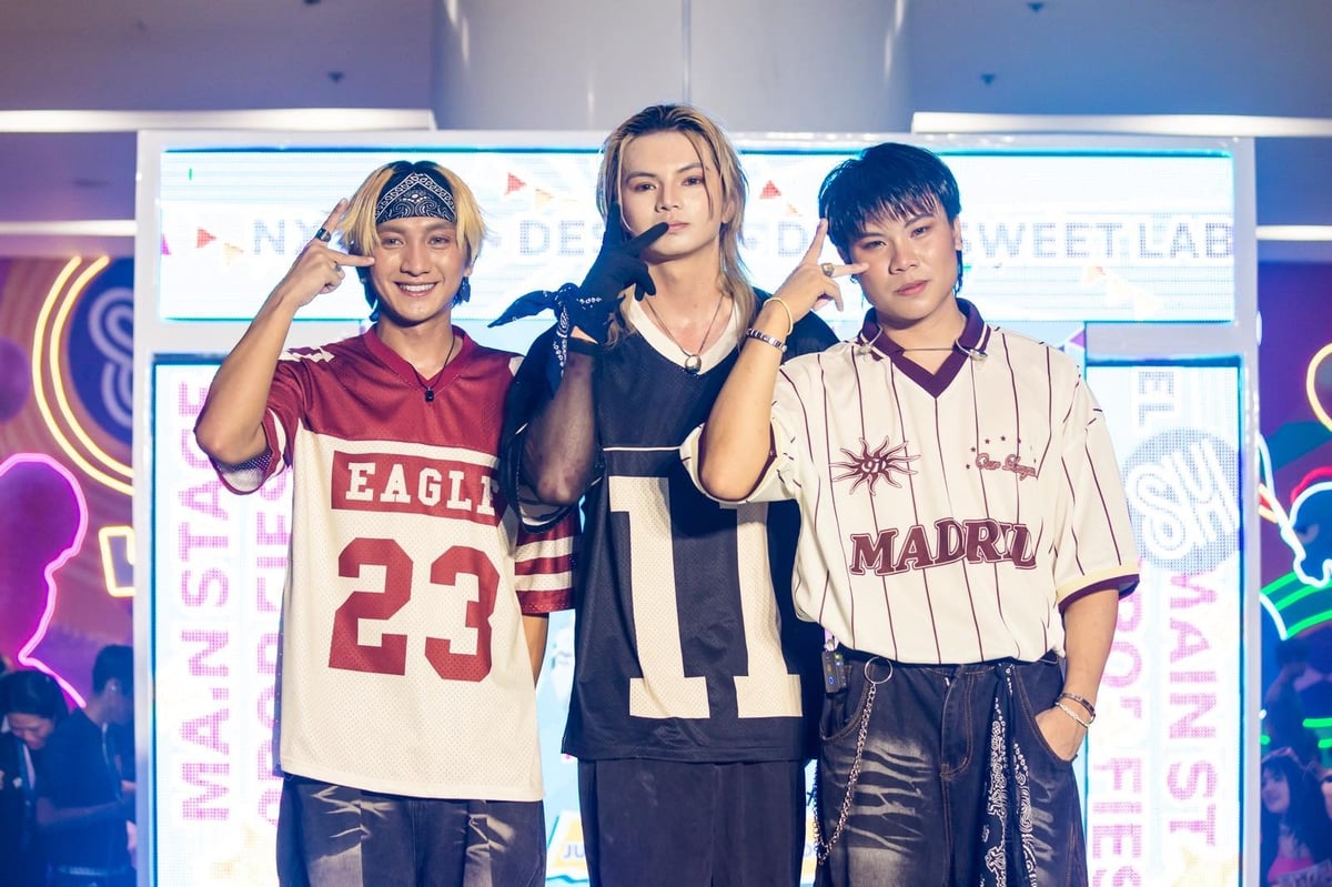 Three people posing on stage in front of neon-lit backdrop wearing sports-inspired jerseys