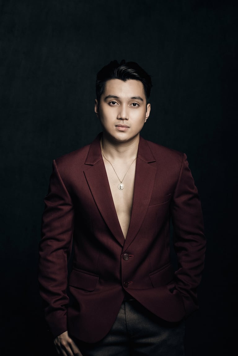 Professional portrait of an Asian man wearing a burgundy blazer and silver pendant necklace against a dark background