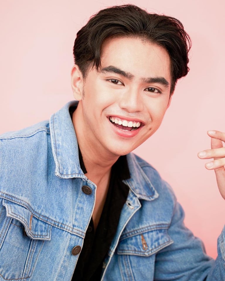 Young man smiling at camera wearing denim jacket over black shirt against pink background