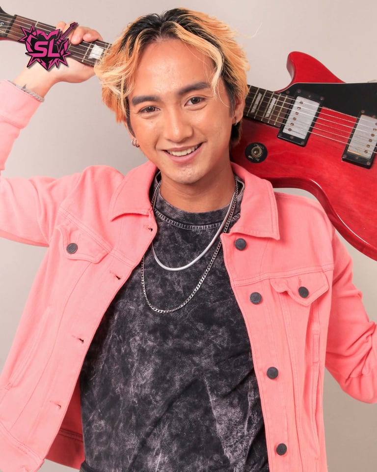 Young man in pink jacket holding red electric guitar against beige background, smiling at camera