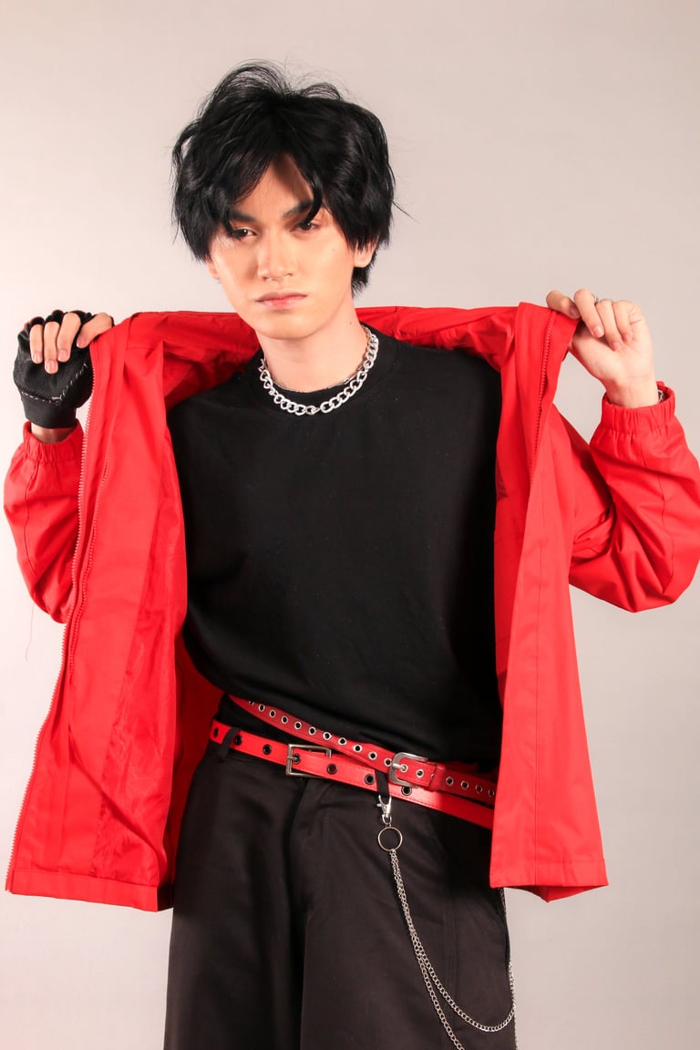 Person with black hair wearing a bright red jacket over black clothing, silver chain necklace, and studded red belt against neutral background