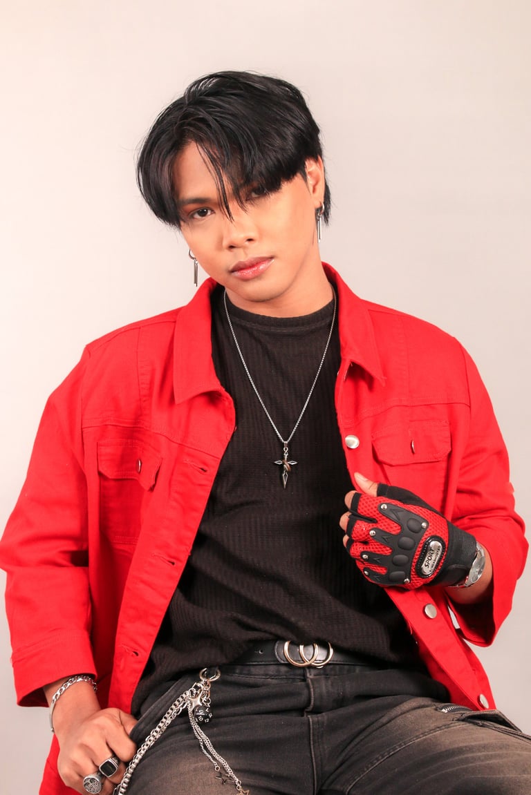 Person wearing a red jacket and black shirt with cross necklace and gloves against neutral background
