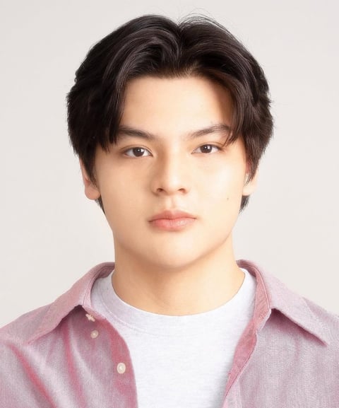 Portrait of a young Asian man with dark hair wearing a pink and white layered shirt against a neutral background