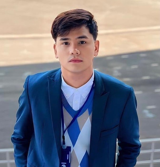 Young man in blue blazer and lanyard posed outdoors against a waterfront background
