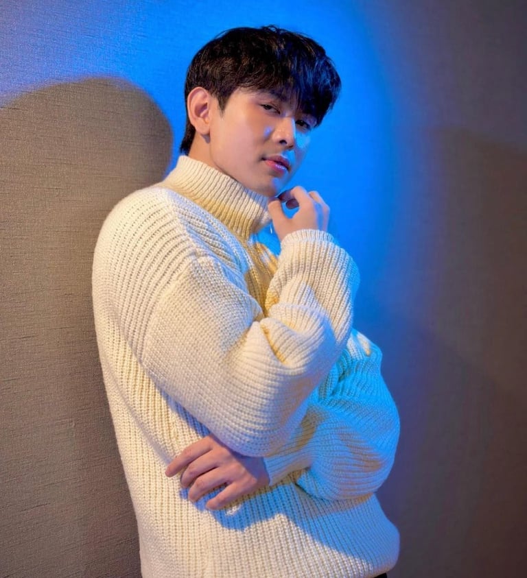 Young man wearing a cream-colored turtleneck sweater posing against a blue-lit background
