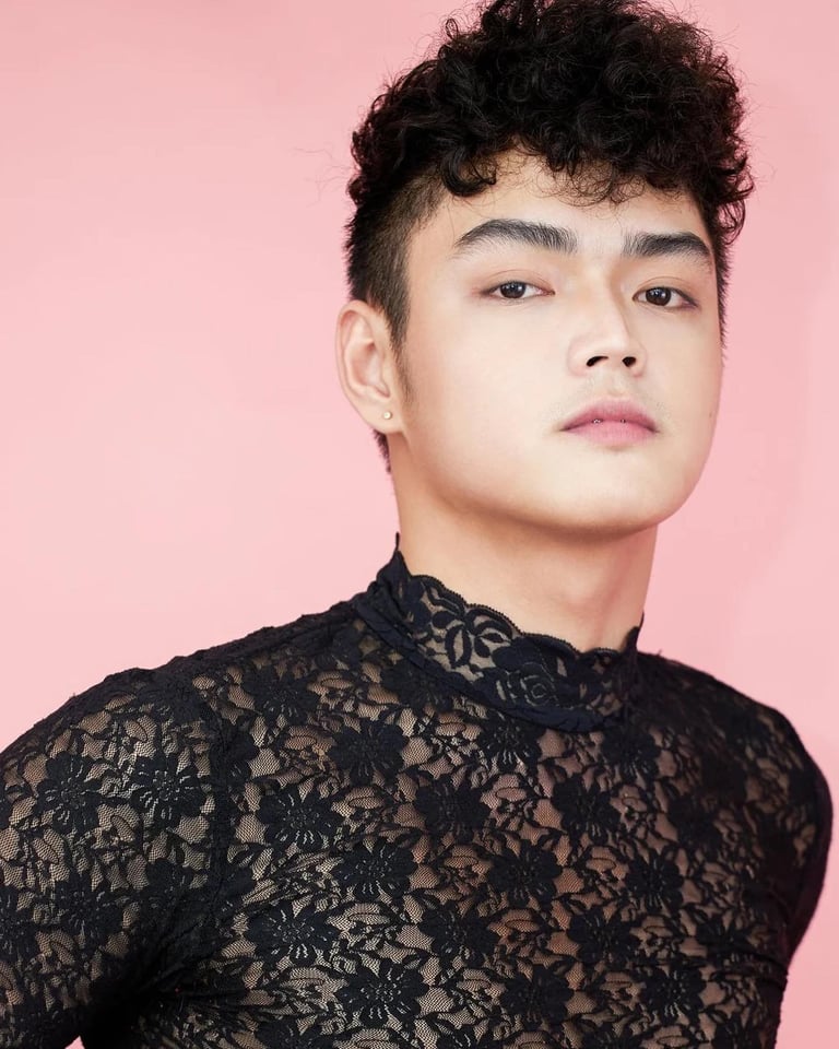 Person with dark curly hair wearing black lace shirt against pink background