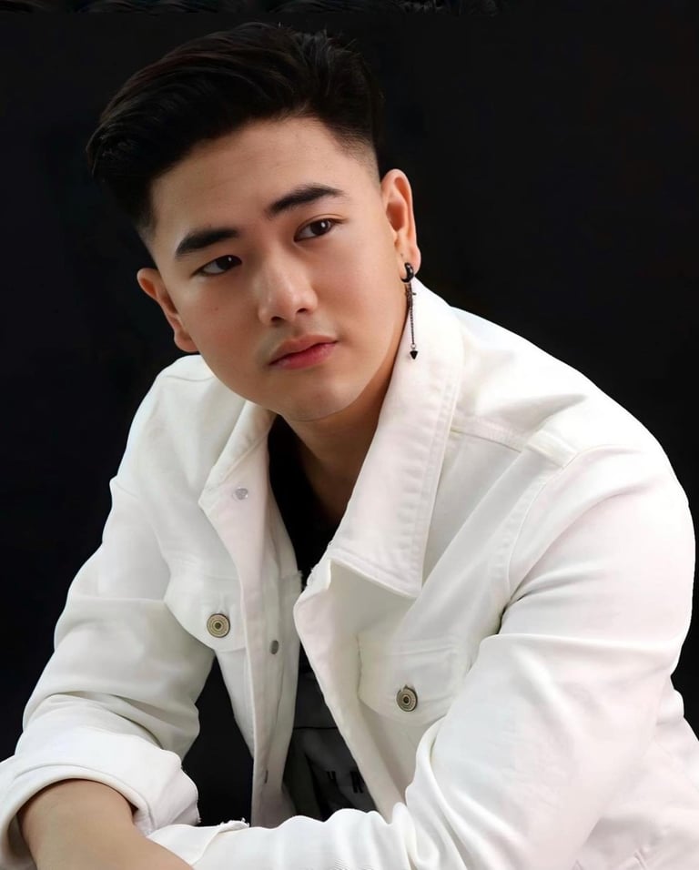 Young man wearing white shirt and earrings against black background, posing for portrait