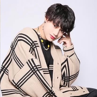 Person wearing a beige and black geometric patterned cardigan with layered gold necklaces, posed against a light background