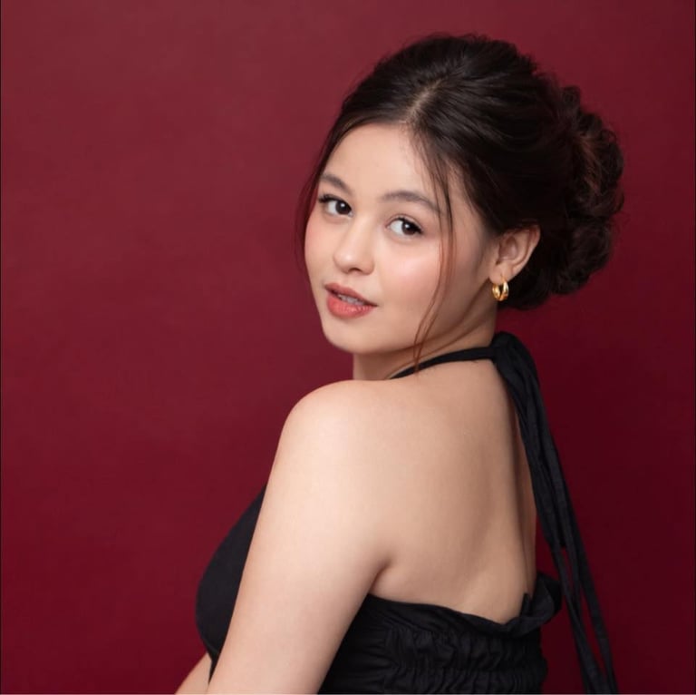 Woman with dark hair in updo wearing black halter top, posed against burgundy background, looking over shoulder