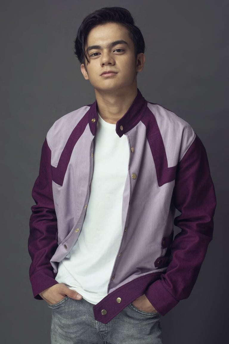 Young man wearing a purple and lavender color-block jacket over a white t-shirt and gray jeans against a neutral background