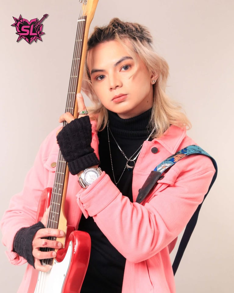Young musician in pink jacket holding red electric bass guitar against neutral background
