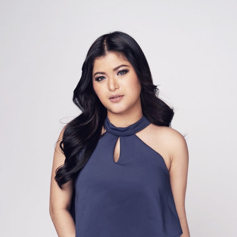 Woman with long black wavy hair wearing a navy blue sleeveless top with keyhole neckline against a light gray background