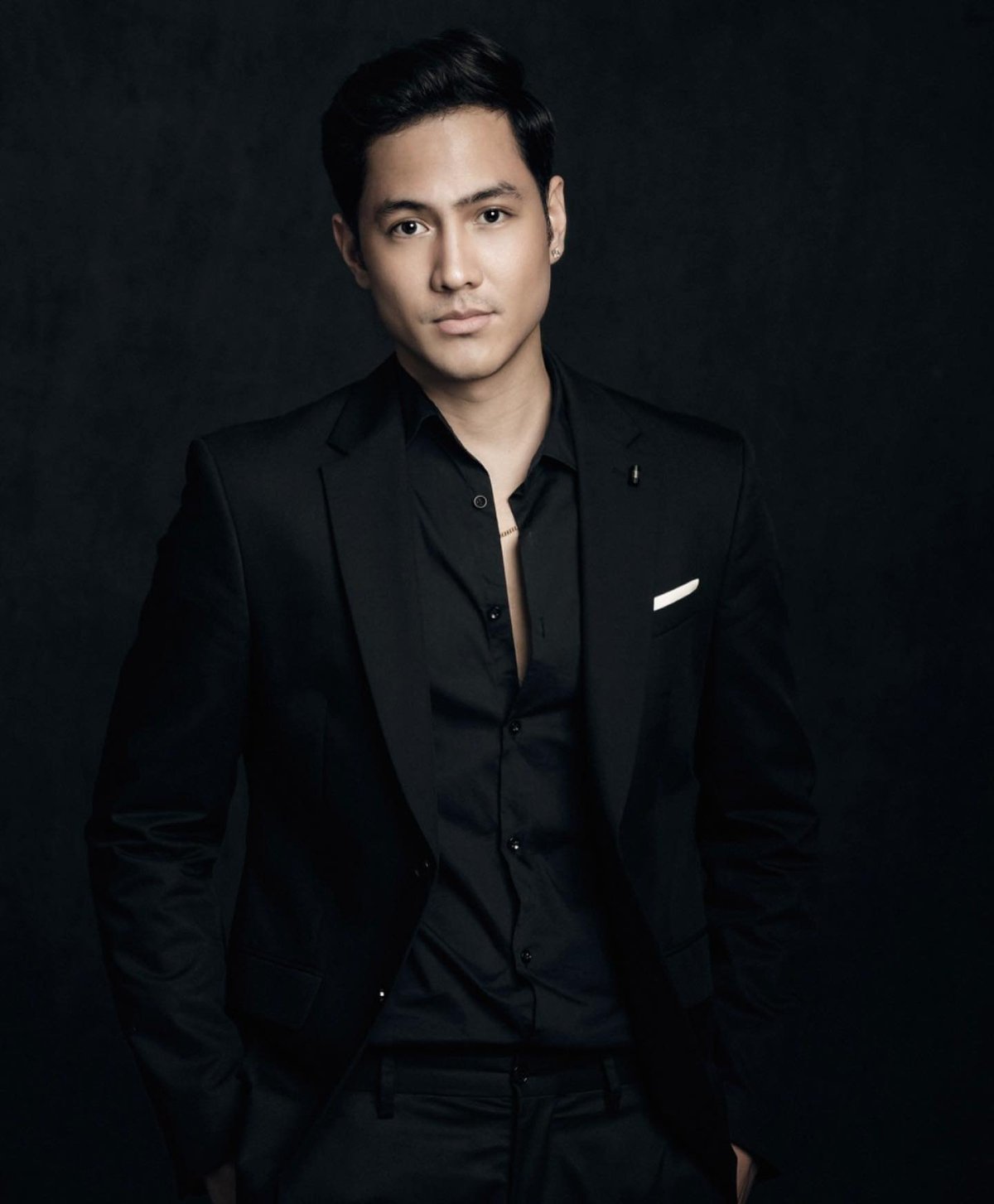 Professional portrait of an Asian man wearing a black blazer and shirt against a dark background