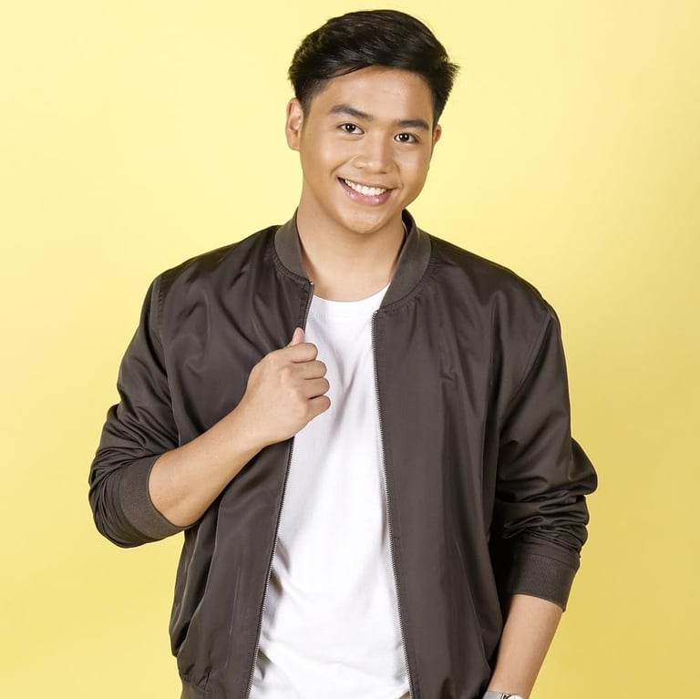 Smiling young man wearing a dark gray jacket over a white shirt against a yellow background