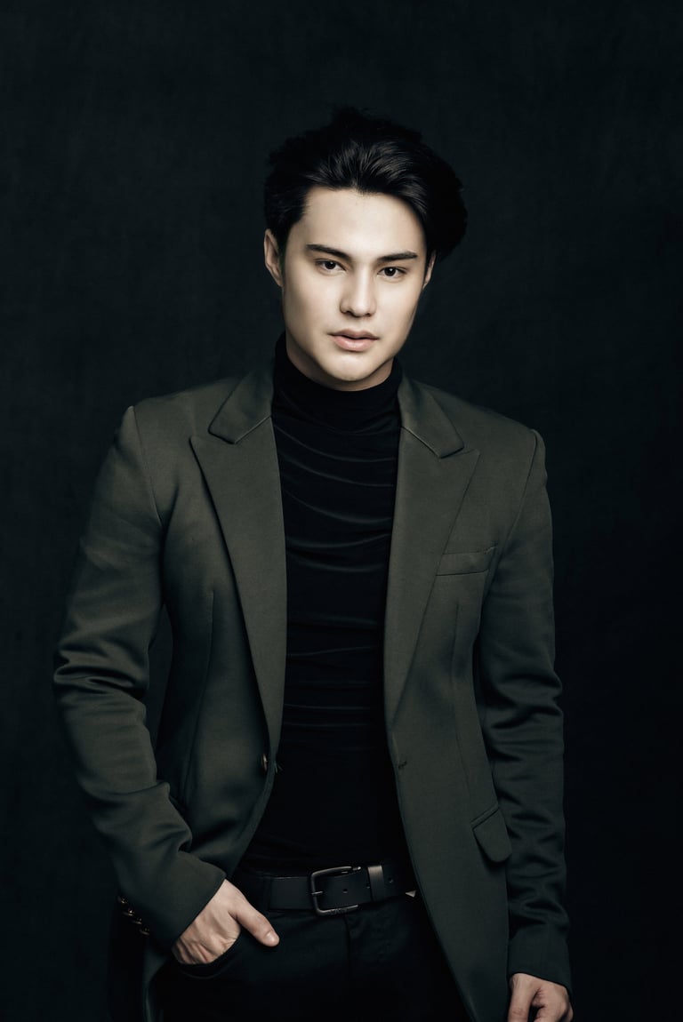 Portrait of a young man wearing an olive green blazer over a black turtleneck against a dark background