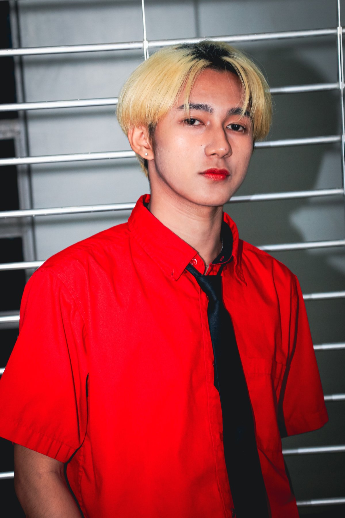 Person with blonde hair wearing bright red shirt and black tie, posed against a geometric gridded background