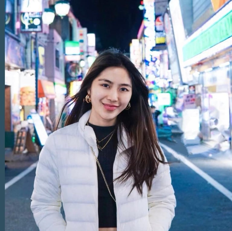 Young woman wearing white puffer jacket smiling at camera on vibrant neon-lit city street at night